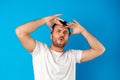 Portrait of a confused young man holding hands on his head over blue background Royalty Free Stock Photo