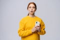 Portrait of confused young woman wearing yellow sweater holding mobile phone and looking at camera Royalty Free Stock Photo