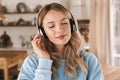 Portrait of content blond girl 20s wearing headphones listening to music at home Royalty Free Stock Photo