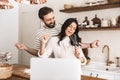 Portrait of content couple looking at laptop while cooking pastry in kitchen at home