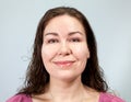 Portrait of a contented, kind woman with long curly hair, grey background, emotions series Royalty Free Stock Photo