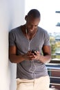 Cool african american man leaning against wall and listening to music with smart phone Royalty Free Stock Photo