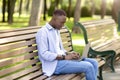 Portrait of cool black guy using laptop on bench at park, working remotely, communicating on webcam Royalty Free Stock Photo