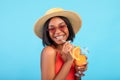 Portrait of cool black woman in swimsuit, straw hat and sunglasses drinking exotic summer cocktail on blue background Royalty Free Stock Photo