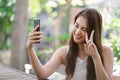 Portrait of cool cheerful Asian girl smile and showing peace sign while taking selfie photo on cellphone in the park. People Royalty Free Stock Photo