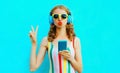 Portrait cool girl blowing red lips sending sweet air kiss holding phone listening to music in wireless headphones on colorful