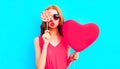 Portrait cool girl with pink heart shaped balloon sending sweet air kiss closing her eye with lollipop on colorful blue Royalty Free Stock Photo