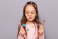 Portrait of cool little girl covered with colorful stickers wearing pink shirt, choosing toothbrush, dental care, standing