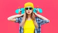 Portrait cool woman with skateboard wearing colorful yellow hat on pink