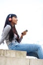 Cool young Indian woman sitting outside with mobile phone and headphones Royalty Free Stock Photo