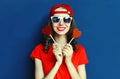 Portrait cool young woman with heart shaped red lollipop wearing baseball cap, sunglasses over blue wall Royalty Free Stock Photo