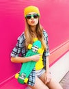 Portrait cool young woman with skateboard blowing lips as air kiss wearing colorful yellow hat on pink