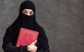 Portrait with copy space adult beautiful Muslim woman wearing black headscarf, traditional dress, reading, holding scripture book Royalty Free Stock Photo