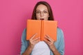 Portrait with copy space for advertisement, studio shot of impressed astonished girl in eyewear holding open notepad in hands,