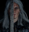 Portrait of cosplayer in image of character Geralt of Rivia from the game or film The Witcher with sword in his arms