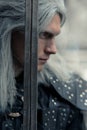 Portrait of cosplayer in image of character Geralt of Rivia from the game or film The Witcher with sword in his arms