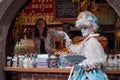 Portrait of Costumed woman with blue dress and fan in front of traditional alsatian store at the Venetian Parade in Riquewihr in A