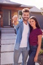 Portrait Of Couple Standing Outdoors In Front Of House With For Sale Sign In Garden Holding Keys Royalty Free Stock Photo