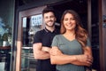 Portrait Of Couple Starting New Coffee Shop Or Restaurant Business Standing In Doorway