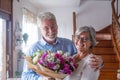 Portrait of couple of two happy and in love seniors or mature and old people holding flowers at home looking at the camera. Royalty Free Stock Photo