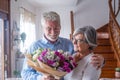 Portrait of couple of two happy and in love seniors or mature and old people holding flowers at home looking at the camera. Royalty Free Stock Photo