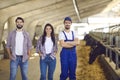 Portrait of a couple of young farmers people together with a farm worker in a cowshed. Royalty Free Stock Photo