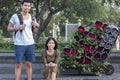 portrait couples of younger asian traveling man and woman sitting at road side beside red roses flower bouquet