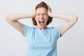 Portrait of crazy hysterical young woman in blue tshirt with closed eyes and hands on head looks stressed and screaming isolated