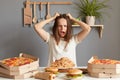 Portrait of crazy irritated shocked woman wearing white T-shirt sitting at table in kitchen, pulling her hair, a girl on a diet, Royalty Free Stock Photo