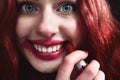 Portrait of crazy-looking teen girl with red hair she is smearing red lipstick on her face, horror concept. halloween time