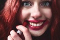 Portrait of crazy-looking teen girl with red hair she is smearing red lipstick on her face, horror concept. halloween time