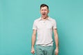 Portrait of crazy weird young man in casual clothes keeping eyes closed, screaming isolated on blue turquoise wall Royalty Free Stock Photo