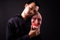 Portrait of crazy young Asian man with hoodie holding horror mask