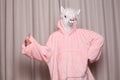 Portrait of creative person in pink hoodie with lama mask showing thumb up against studio wall background