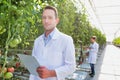 Portrait of crop scientist wearing lab coat while holding clipboard in greenhouse