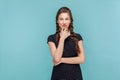 Cunning woman with braids standing holding chin pondering, thinking about devil plan or prank.