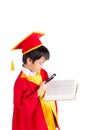 Portrait Of Curious Boy In Red Gown Kid Graduation With Mortarboard Looking A Book Through Magnifying Glass Royalty Free Stock Photo