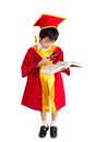 Portrait Of Curious Boy In Red Gown Kid Graduation With Mortarboard Looking A Book Through Magnifying Glass Royalty Free Stock Photo