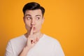 Portrait of curious cunning speechless guy finger close lips look empty space on yellow background