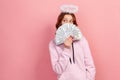 Portrait of curious curly haired teenage girl in hoodie with halo on head hiding face with bunch of dollar banknotes and looking