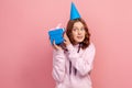 Portrait of curious curly haired teenage girl in hoodie with party hat holding wrapped gift box Royalty Free Stock Photo