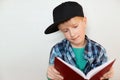 A portrait of curious little boy in black cap and checked colorful shirt reading encyclopedia looking into the book with interest. Royalty Free Stock Photo