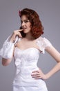 Portrait of Curious Redhaired Caucasian Female Posing in White Wedding Dress and Little Purse Against Gray Background