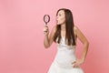 Portrait of curious shocked bride woman in white wedding dress looking aside through magnifying glass on pastel
