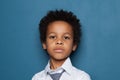 Portrait of curious smart black child boy student on blue background. African American kid pupil 6 years old