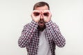 Portrait of curious wondered bearded man looking through fingers gesturing binoculars. white background