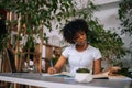 Portrait of curly African-American young woman in earphones writing notes, watching webinar, studying online using Royalty Free Stock Photo