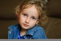 Portrait of a curly blue-eyed girl with a calm look. She is wearing a denim vest