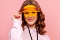 Portrait of curly haired teenage girl in hoodie touching yellow sun visor cap and sincerely smiling on camera, close-up view Royalty Free Stock Photo