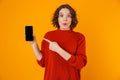 Portrait of curly woman holding and demonstrating smartphone while standing isolated over yellow background Royalty Free Stock Photo